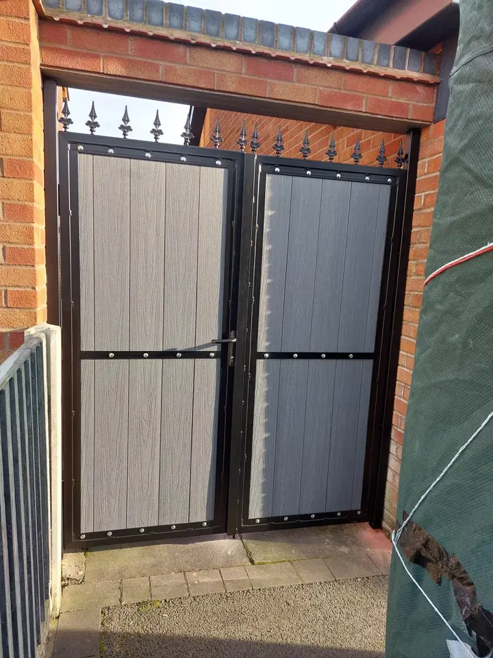 Black steel framed double gate filled with grey boards, fitted in a brick gateway with spear finials on top
