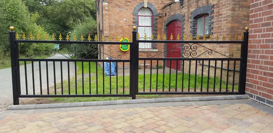 Black railings and gate with gold-coloured finials along a brick-paved frontage