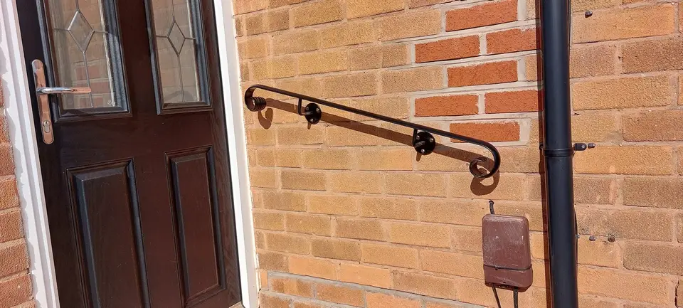 Black wall-mounted handrail with a scrolled end bracket fixed to an orange brick wall