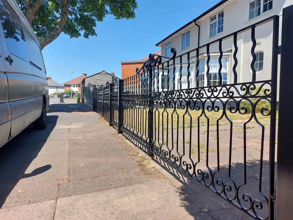 Black scrolled wrought iron railings running along a pavement in front of a white house