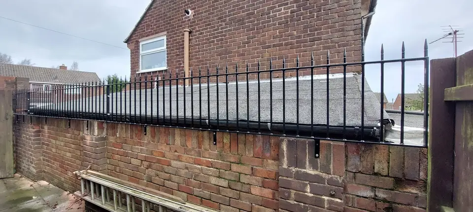 Black spear-topped steel railings fixed along the top of a brick wall beside a flat roof