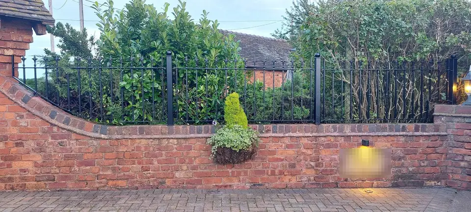 Black spear-topped railings set on a curved brick wall behind a hanging basket