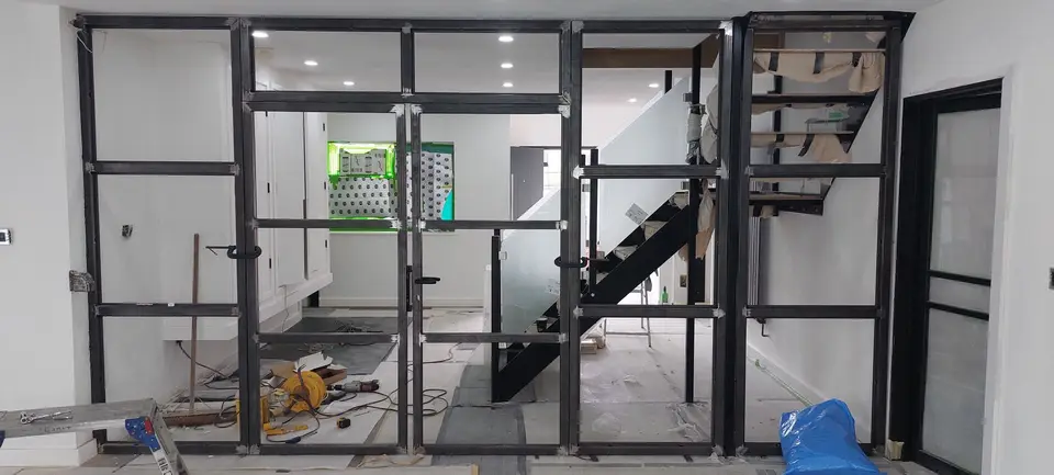 Black steel frame for a glass partition wall during fitting, with a staircase and tools behind