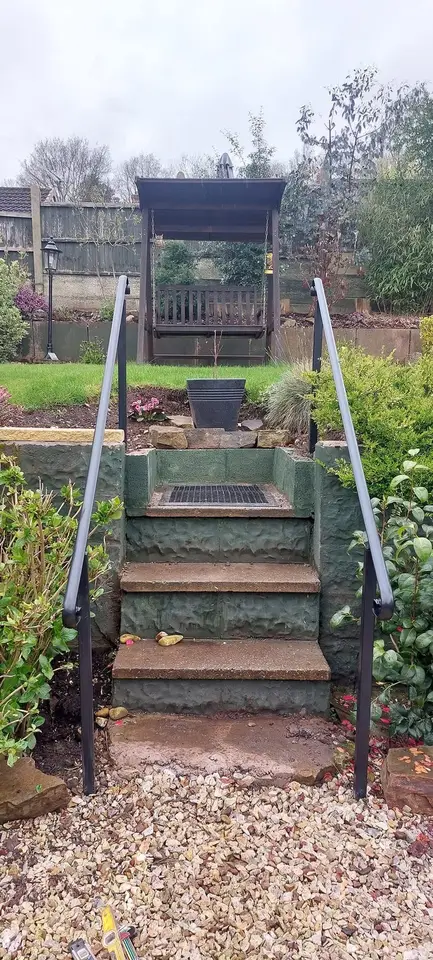 Two slim grey handrails either side of stone garden steps leading up to a lawn