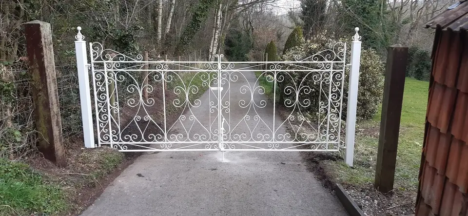 White double driveway gates with heart-shaped scrollwork, closed across a tarmac track