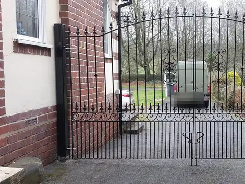 Black arched double gates with spear finials and scrollwork along the bottom rail, fitted between two brick walls