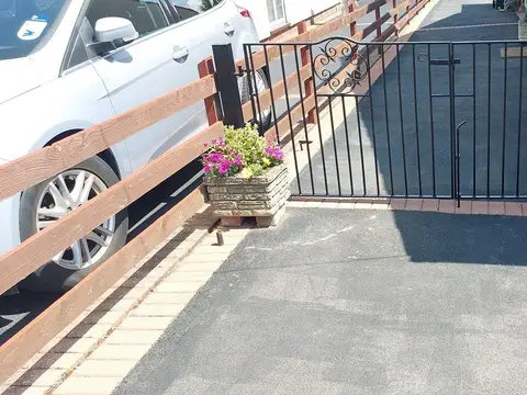 Black bar driveway gate with a scroll detail in the top corner, set across a narrow tarmac drive