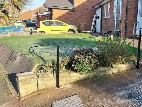 Slim black handrail with a curled end on posts beside a sloping garden path