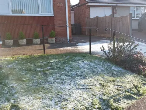 Slim black handrail with curled ends crossing a frosted lawn to a white front door