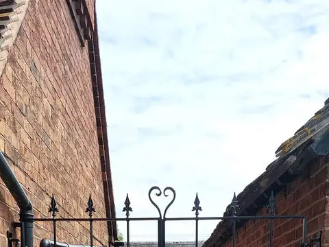 Black double side gate with a heart-shaped finial in the centre, between two brick walls