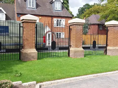 Black railings and a gate between brick piers with stone caps, in front of a white house