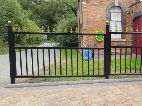 Black railings and gate with gold-coloured finials along a brick-paved frontage