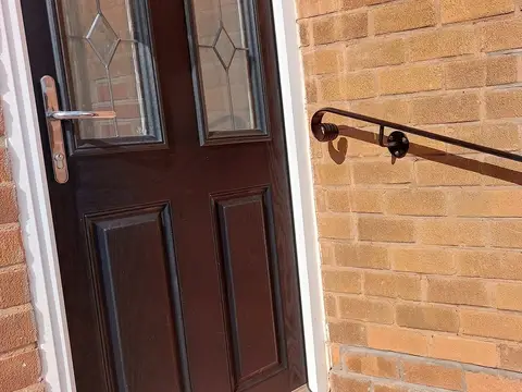 Black wall-mounted handrail with a scrolled end bracket fixed to an orange brick wall