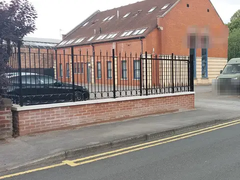 Black scroll-topped railings on a low brick wall beside a quiet road