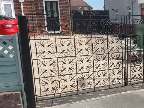 Black driveway gates filled with repeating scrollwork panels, fitted across a front garden