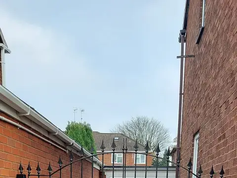 Black double gate with spear finials closing a drive between a brick wall and a house, garage door behind