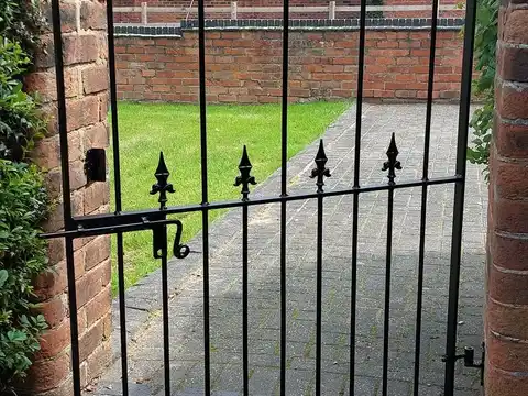 Black single gate with spear tops and a thumb latch, hung in a brick opening beside a lawn