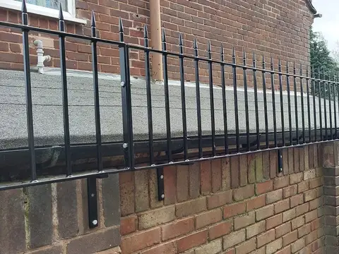 Black spear-top railings bolted to a brick wall above a flat roof, seen from the side