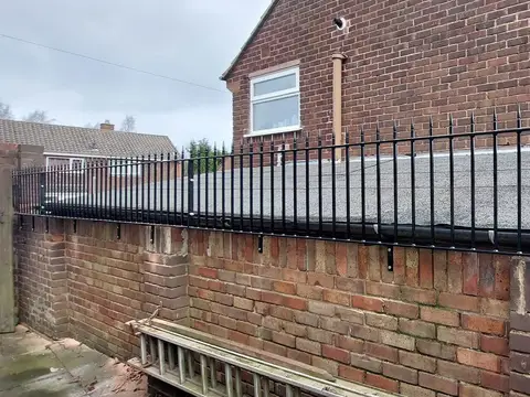Black spear-topped steel railings fixed along the top of a brick wall beside a flat roof