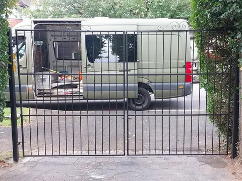 Black square bar double gates with a scroll top rail, hung between ivy-covered hedges