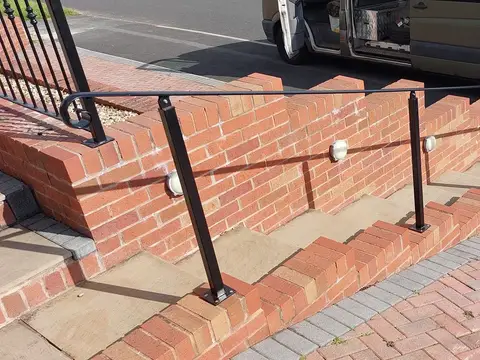 Black handrail on square posts fixed along brick-edged steps beside a block-paved drive