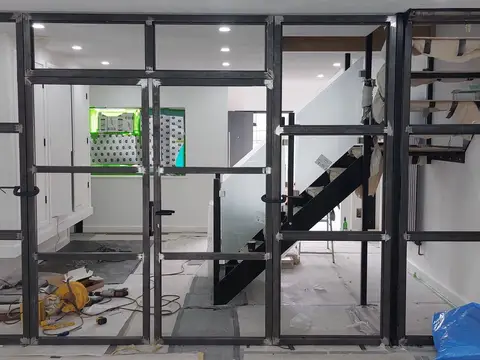 Black steel frame for a glass partition wall during fitting, with a staircase and tools behind