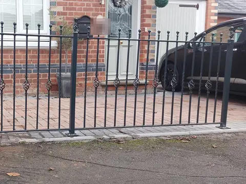 Grey steel railings with basket-twist detail along the front of a brick house and drive