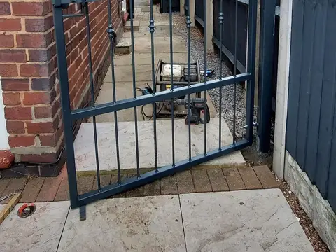 Dark grey steel side gate closing the passage beside a brick house