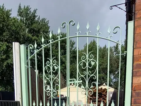 Mint green arched pedestrian gate with scrollwork and spear finials, set between painted posts