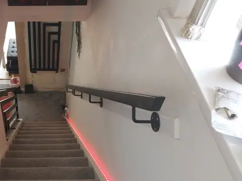 Wall-mounted black handrail running down a stairwell with a pink LED strip below it