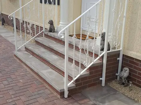 White steel handrails with scrolled balusters beside brick porch steps