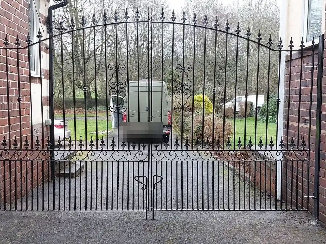 Black arched double driveway gates with spear finials and scrollwork along the bottom rail, made and fitted by MP Gates and Handrails